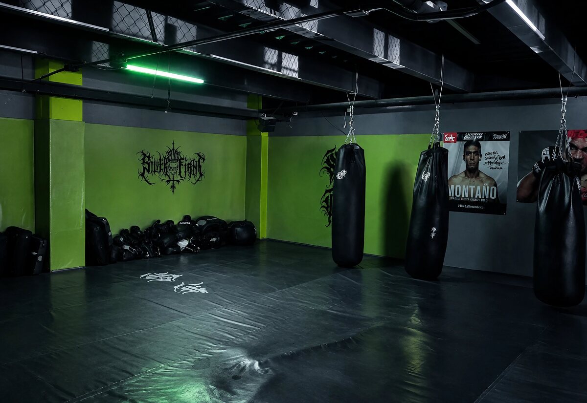 Salón de kick boxing con costales y luz verde en Silver Force Gym